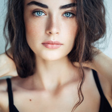 Hübsche junge Frau mit dunklen langen Haaren und blauen Augen schaut in die Kamera